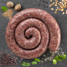 Load image into Gallery viewer, Raw sausage coil on a dark surface with various seasonings and herbs.